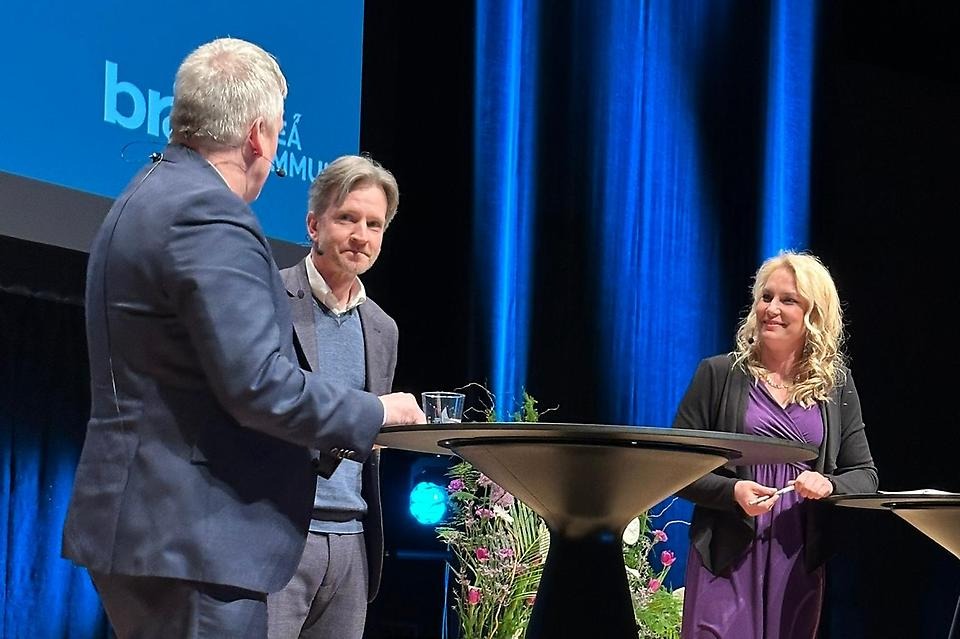 Två män och en kvinna samtalar på en scen.