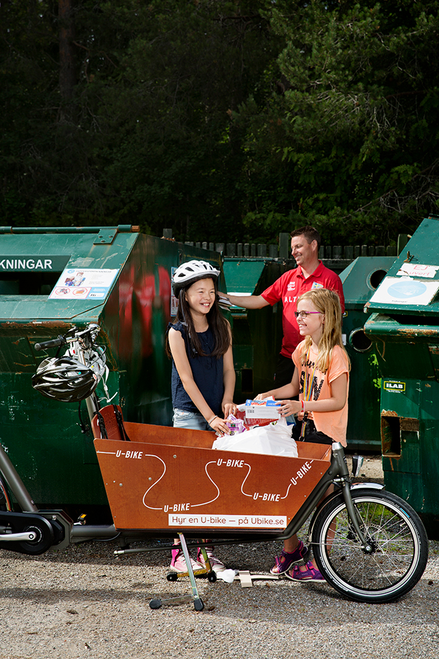 Två barn och en vuxen som lämnar återvinning med en lådcykel i förgrunden.