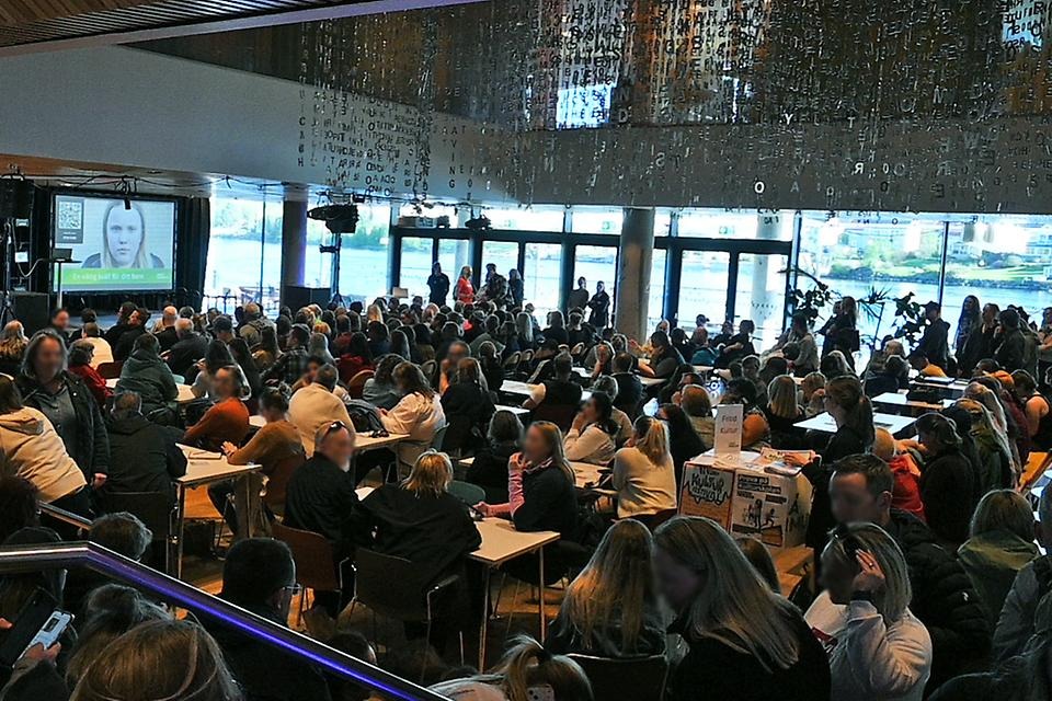 Fullt med folk i lokal med utsikt över större vattendrag. En presentation visas på en storbildsskärm där en flickas ansike finns i bild.