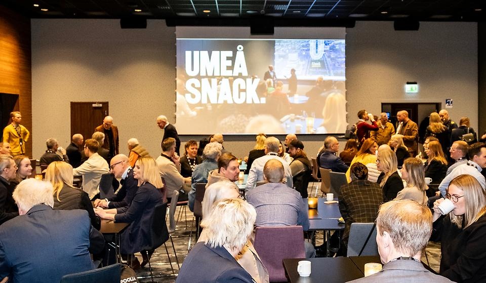 Sal med många människor i rörelse. På stor skärm finns bild med texten Umeå snack.