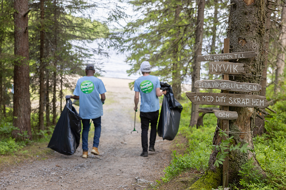 Två personer går längs en stig mot en strand med soppåse och skräpplockare i handen