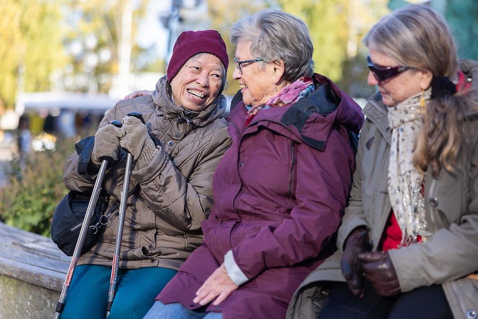 Vänner som sitter på en bänk och ler mot varandra