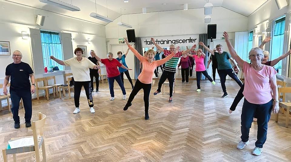 Många seniorer tränar tillsammans i stor lokal med parkettgolv.