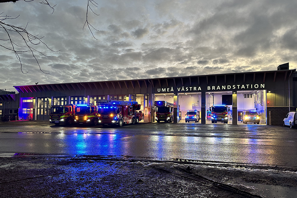 Flera brandbilar med blåljus framför en brandstation