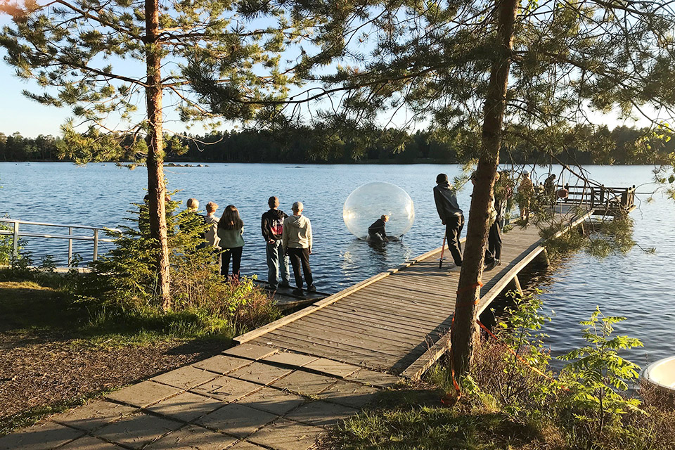 Ungdomar står vid strandkanten och tittar på en person som testar en vattenboll.