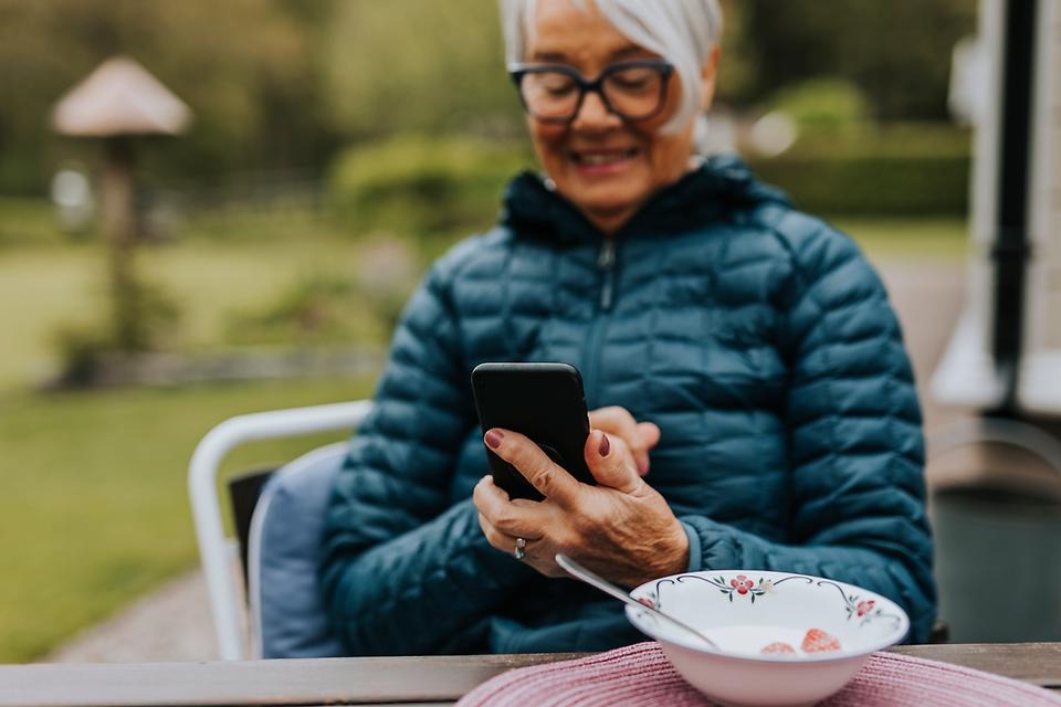 Kvinna som sitter utomhus och tittar i sin mobiltelefon.