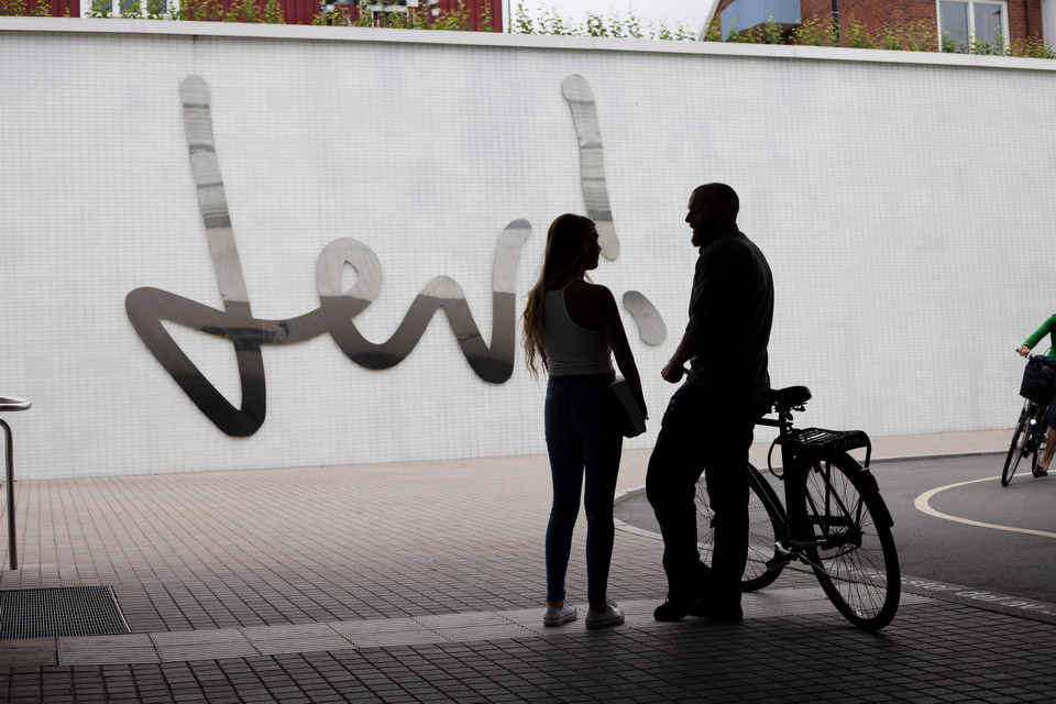 A young man and woman talking, outside next o a bicycle.
