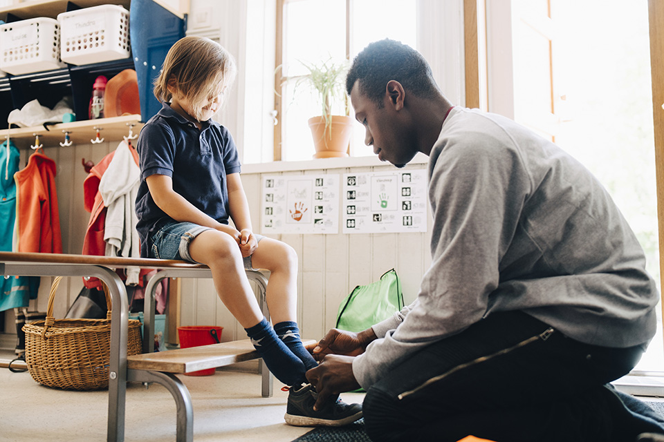 Preschool teacher helps a child with his shoes.