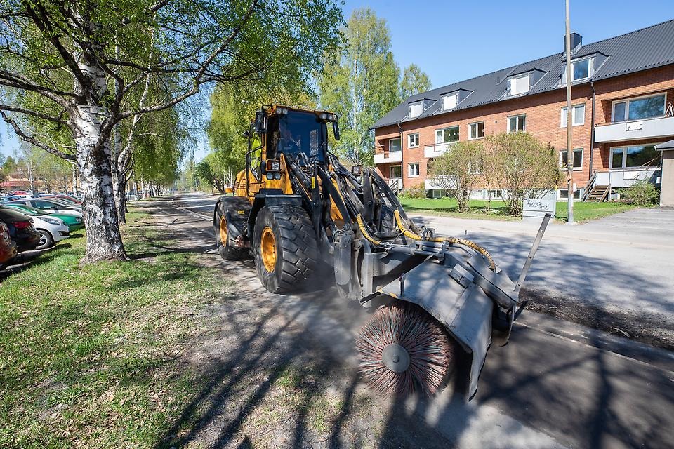 Gul traktor sopar gata och trottoar rena från grus.
