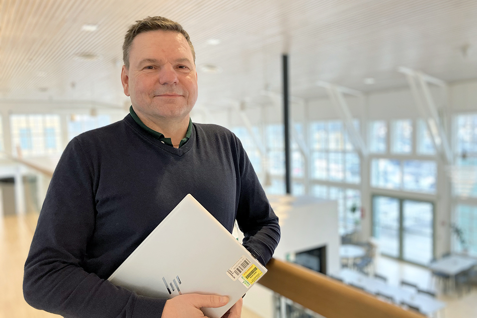 En person står i en stor lokal med en laptop i handen.