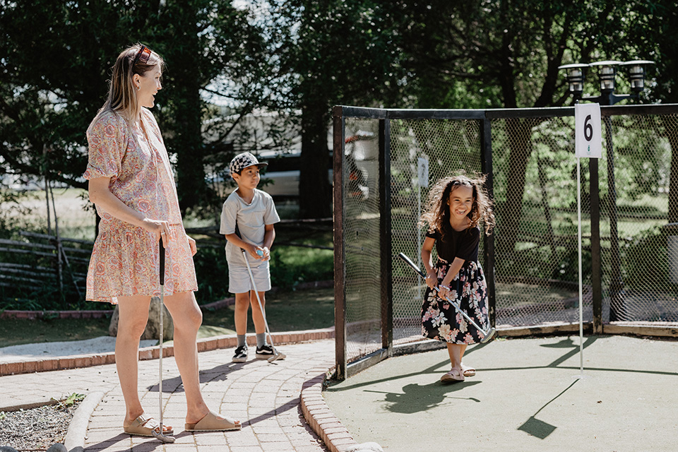 En mamma spelar minigolf med sitt barn och barnets kompis