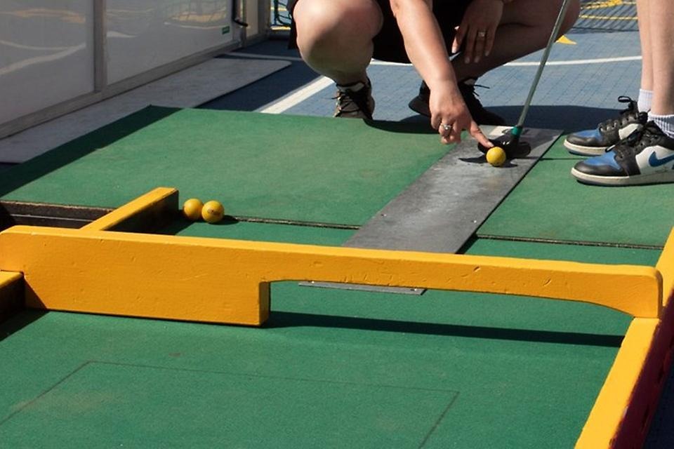 Grön minigolfbana i närbild med gula bollar och ett klubbhuvud.
