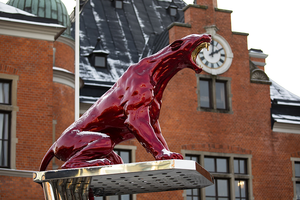 Konstverk med rött kattdjur som sitter på en ställning av stålrör.