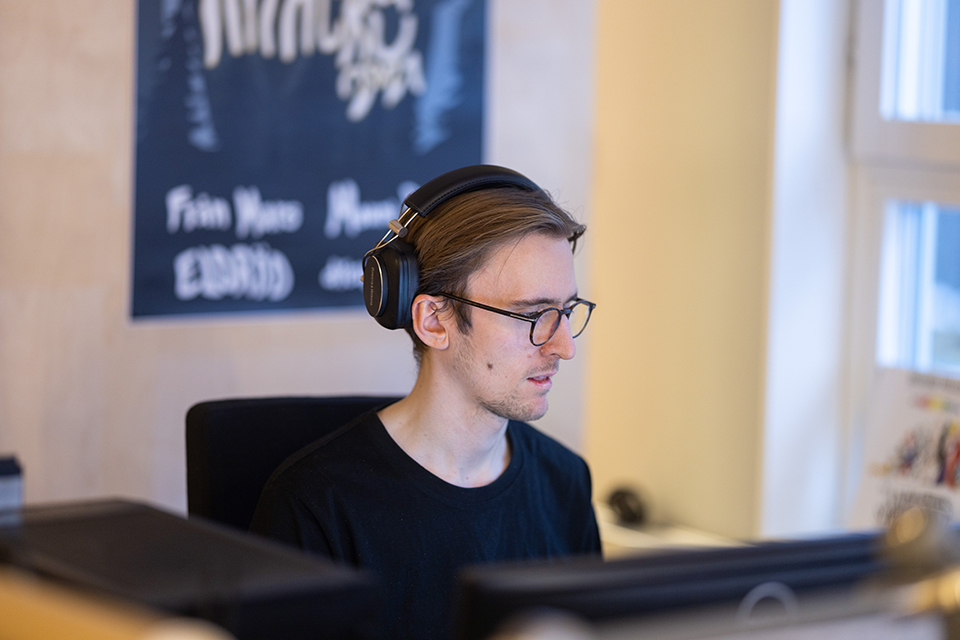 Bilden visar Erik som sitter vid en dator med hörlurar på huvudet.