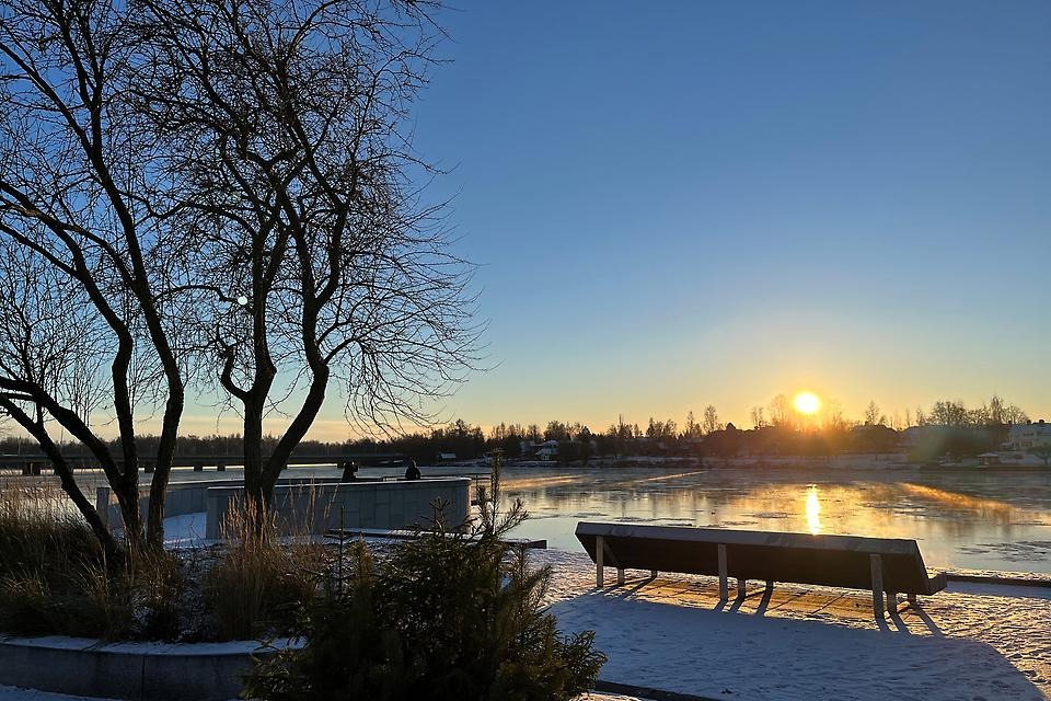 Vacker vinterbild med en parkbänk med utsikt mot Umeälven i solnedgång