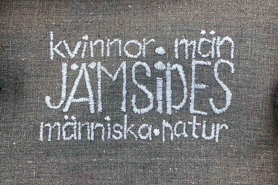 Skydd i tyg för kommunfullmäktiges nya ordförandeklubba, med text "kvinnor ● män JÄMSIDES människa ● natur".