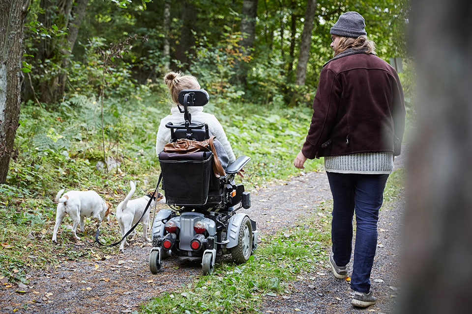 En kvinna i rullstol är ute i skogen med sina hundar tillsammans med en man