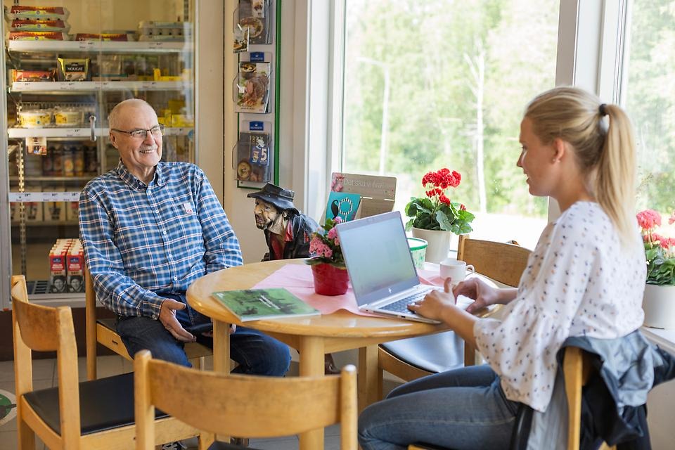 Man och kvinna samtalar vid bord och skriver på en laptop