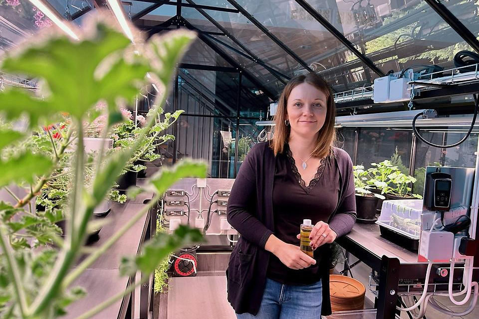 Regina poserar på jobbet framför gröna växter.