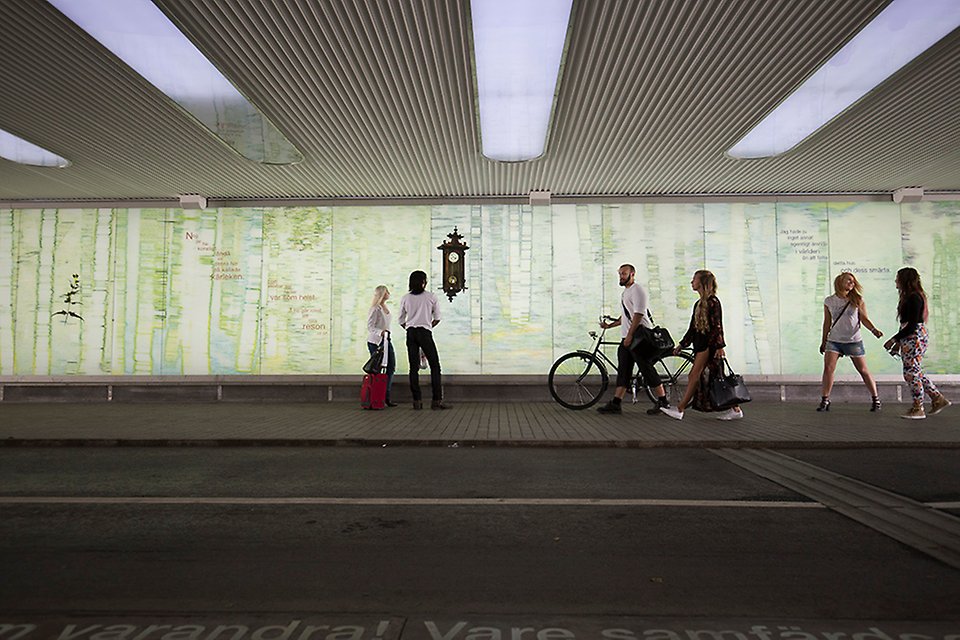 Människor i rörelse i ljus gångtunnel med konst på väggarna.