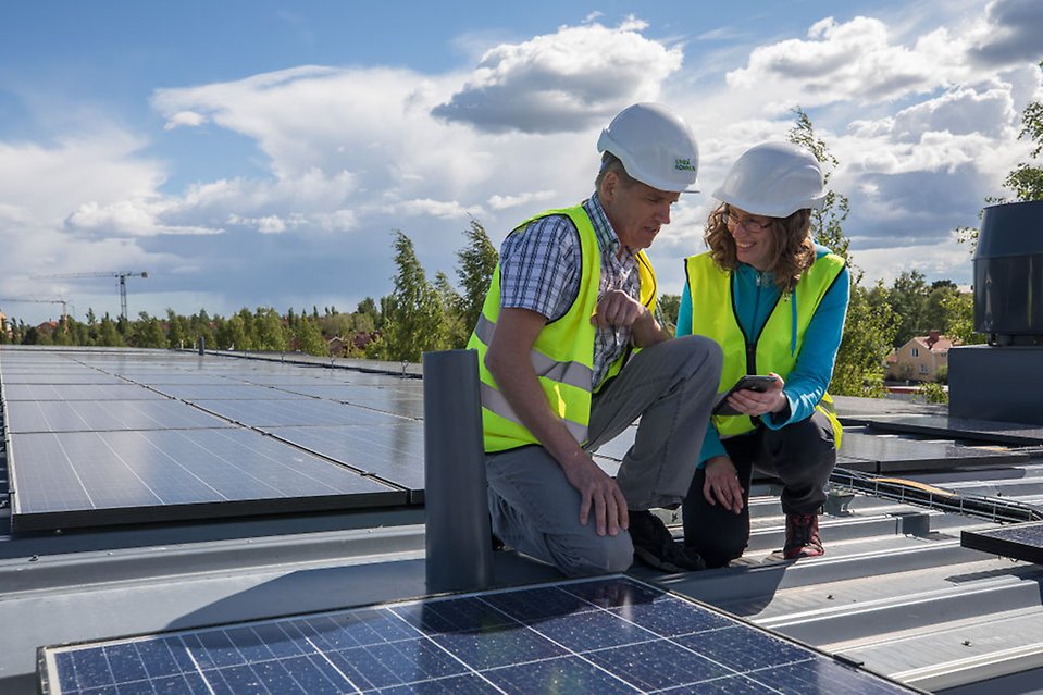 En kvinna och en man med arbetshjälmar mäter effekt av solceller på ett tak.