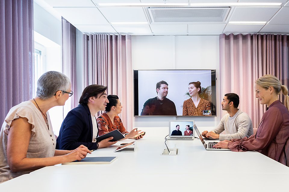 Människor som sitter runt ett mötesbord och har ett digitalt möte.