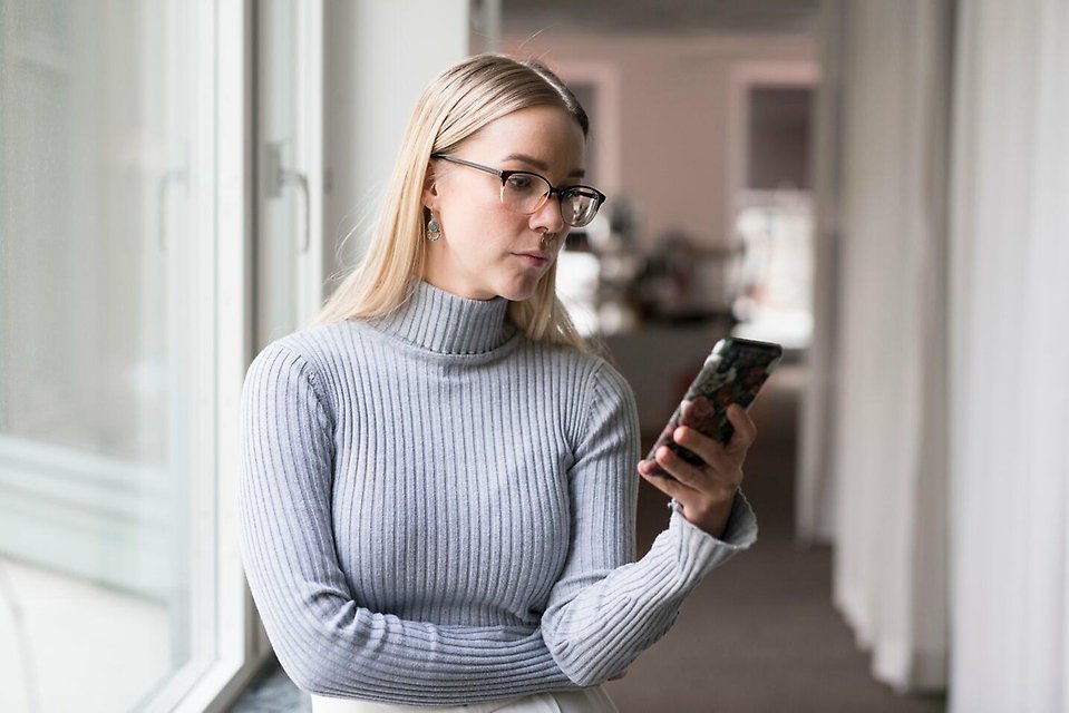 Kvinnor kollar på mobiltelefon, bussar i bakgrunden